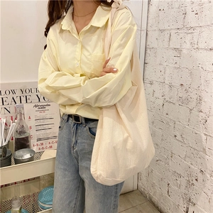 Detail showing a minimalist beige canvas tote bag paired with a soft yellow cotton shirt