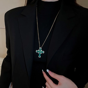 Détail du pendentif croix en zircon vert avec chaîne dorée sur une veste blazer noire