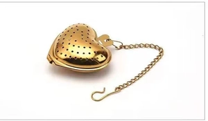 Detailopname van de gouden hartvormige thee-ei met metalen ketting op wit