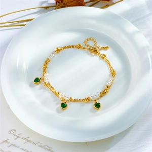 Elegant gold double-layer anklet with green heart pendants and clear beads on white tray