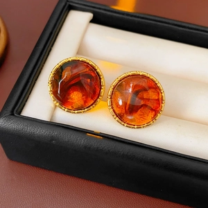 Macro shot of amber resin stud earrings with golden gear borders in a premium gift box