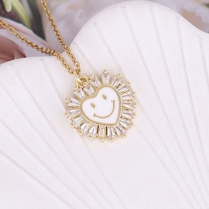 Macro detail of gold heart pendant with zircon border and white enamel smiley face