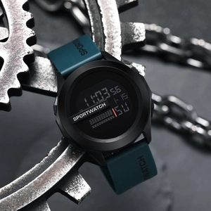 Digital sports watch with large round dial and teal strap on an industrial gear background