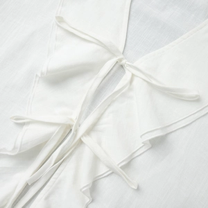 Detail of white cotton blouse showing ruffled V-neck and delicate bow tie closures