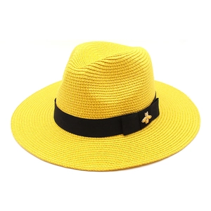 Close-up of bright yellow woven straw Fedora hat with black ribbon and gold bee buckle
