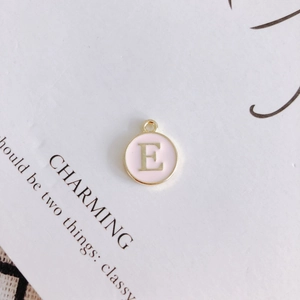 Detail of round pink enamel letter E pendant with gold finish for DIY jewelry making
