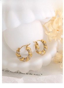 Detail of gold U-shaped twist hoop earrings with white zircons on shell stand