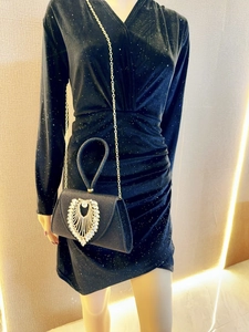 Detail of a black evening clutch with a sparkling heart rhinestone and gold chain strap