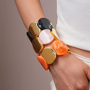 Dettaglio del bracciale largo elastico con pezzi in metallo dorato e resina marmorea