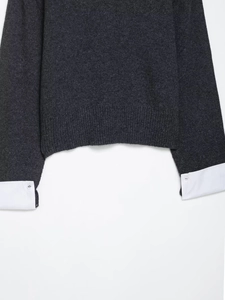 Detailed view of dark grey knit sweater with white shirt cuff contrast and button details