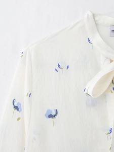Detailed view of white floral blouse neckline with blue prints and ribbon bow tie