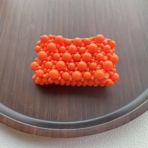 Detail of vibrant orange beaded texture with multi-size resin spheres on dark wood