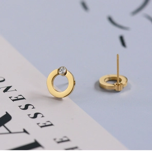 Macro detail of geometric gold-plated hoop earrings featuring clear sparkling crystal studs