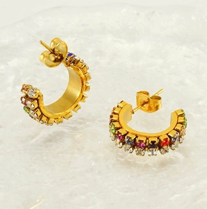 Macro view of C-shaped gold-plated earrings with colorful zircon stones on textured glass