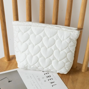 Detail of white heart quilted makeup bag with zipper on a wooden chair with magazine
