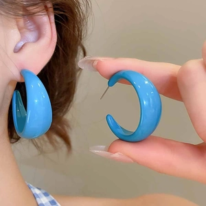 Close-up detail of blue acrylic C-shaped hoop earrings with a glossy finish on model ear
