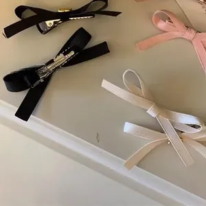 Detailed close-up of ribbon bow hair clips in black, white, and pink with metal duckbill clips