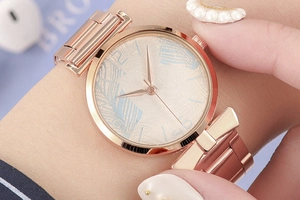 Close-up of rose gold mesh watch featuring a golden textured dial with numeric markers