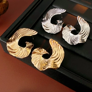 Macro detail of gold and silver curved wave earrings with hammered metal texture