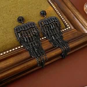Close-up of black long tassel earrings with faceted stones on a green velvet surface