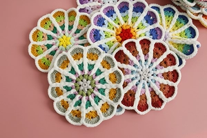 Close-up of handmade gradient crochet coasters in various colors on a soft pink background