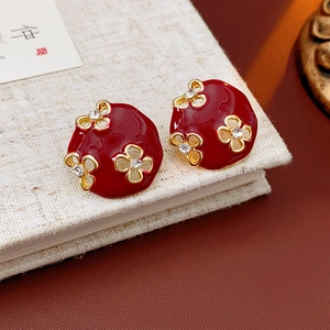 Boucles d'oreilles fleurs C vintage en or avec émail rouge et diamants sur un livre