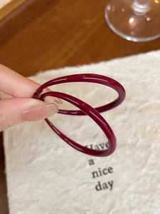 Close-up of hand-held deep red enamel hoop earrings with a glossy finish and silver needle
