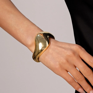 Nahaufnahme eines minimalistischen goldenen Armreifs mit flüssiger Metalltextur und Glanz