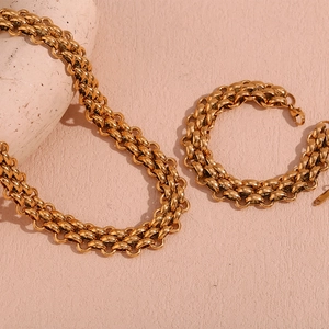 Flat lay of chunky gold necklace and bracelet set on a textured warm pink background