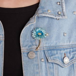 Detailed close-up of blue daisy flower brooch pinned on a stylish denim jacket collar