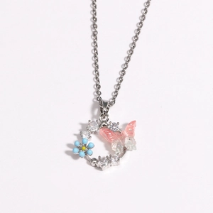 Détail du pendentif couronne fleurie avec fleur bleue et papillon rose sur chaîne argentée