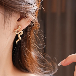 Gros plan d'une boucle d'oreille serpent plaquée or avec zircons portée par un modèle