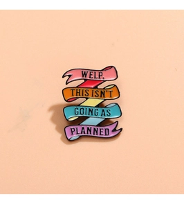 Macro shot of rainbow enamel pin with 'WELP. THIS ISN'T GOING AS PLANNED' humorous quote