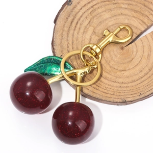 Close-up of sparkling dark red cherry keychain with green glitter leaf and gold hardware