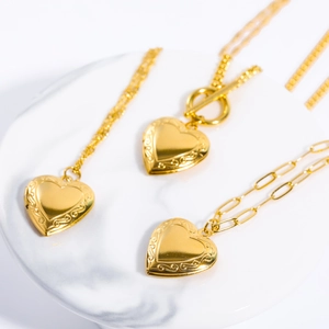 Detailed view of three gold heart locket necklaces with T-bar clasps on marble stand