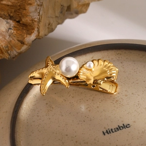 Detailed close-up of a gold starfish and shell hair clip with pearls on a ceramic plate