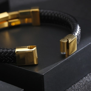 Close-up of black braided leather bracelet with a gold magnetic clasp on dark background