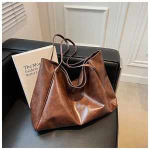Detail of dark brown vintage faux leather tote bag showing soft texture on a black sofa