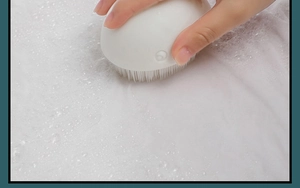 Detail of white whale cleaning brush with dense bristles scrubbing soapy fabric surface