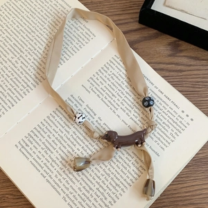 Detail view of cream knit cherry ribbon necklace with dachshund pendant on antique book