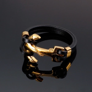 Detail of black leather braided bracelet with polished gold anchor buckle on dark mirror