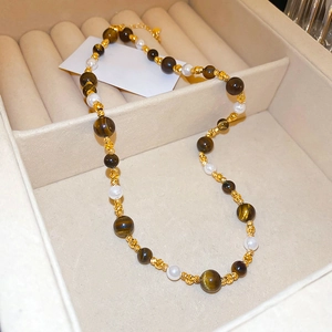 Detailed close-up of tiger eye and pearl beaded necklace in beige jewelry box