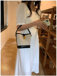 Detail view of the black and white canvas bucket bag worn by a model in a warm interior