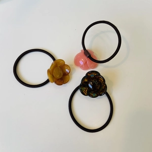 Detailed view of three resin flower hair ties in amber, pink and tortoiseshell colors