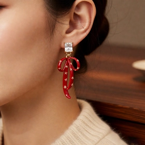 Close-up of vintage bow drop earrings with red glaze and star details on model ear
