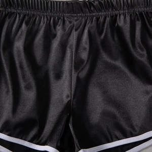Close-up of black satin sports shorts featuring elastic waistband and white contrast piping