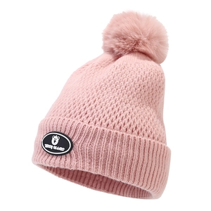 Detail of pink knitted winter beanie with faux fur pompom and teddy bear patch