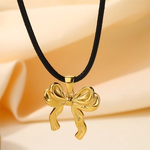 Close-up of golden bow pendant on black cord necklace against beige soft fabric background