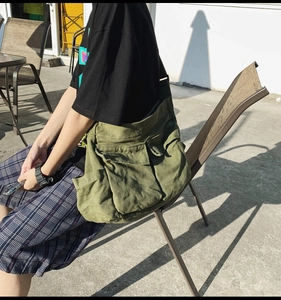Detail of army green canvas messenger bag with multiple exterior pockets shown on model
