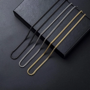 Detail of 3mm box chain necklaces in black, silver, and gold on a matte gift box